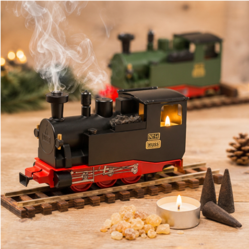 HUSS Incense Train black, locomotive incense burner with smoke rising from the chimney, a glowing tealight, and incense cones on railway tracks with a green version blurry in the back.