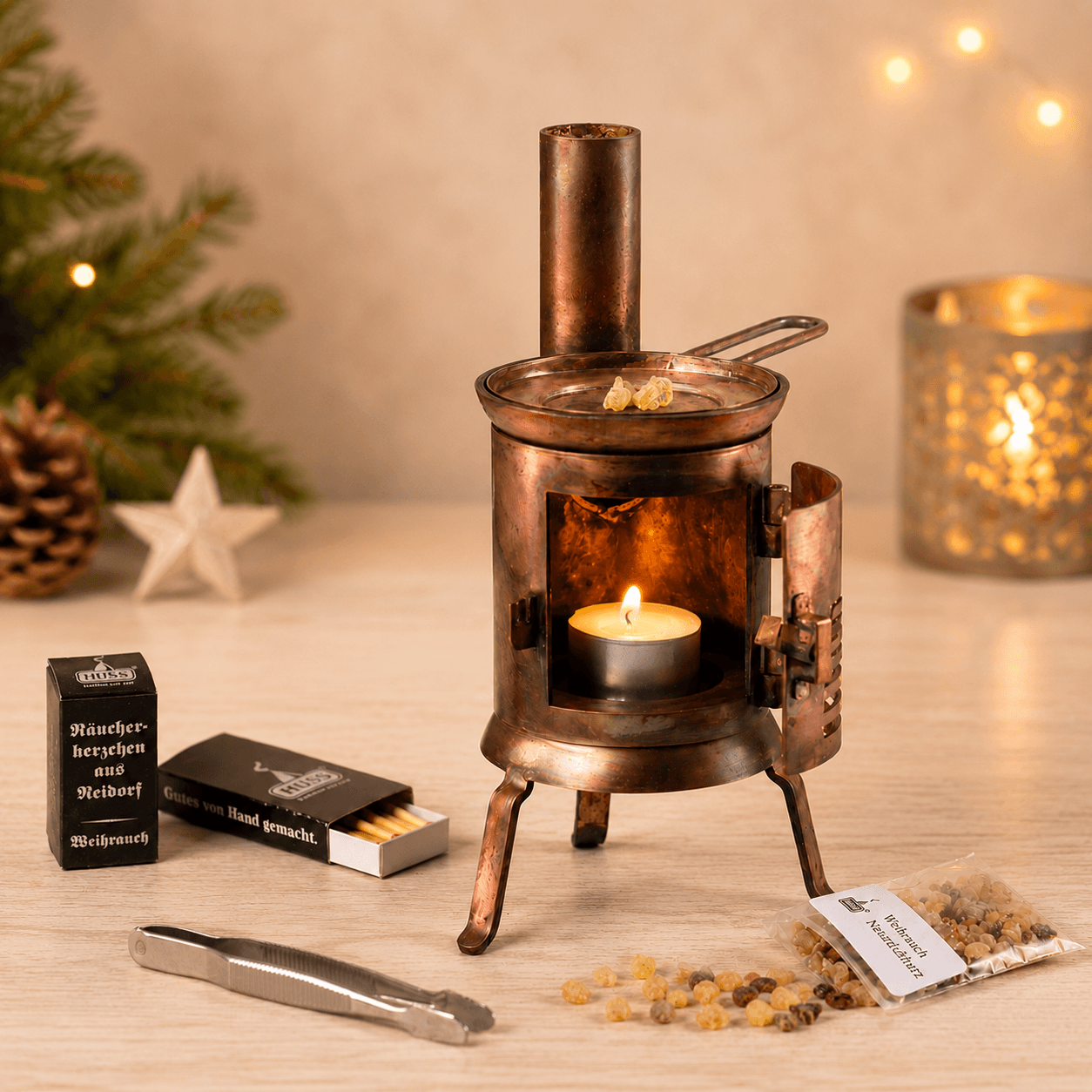 HUSS Incense Table Huss'l a copper oven burner with a lit tealight, natural frankincense resin, and resin accessories displayed on a wooden table with Christmas decor.