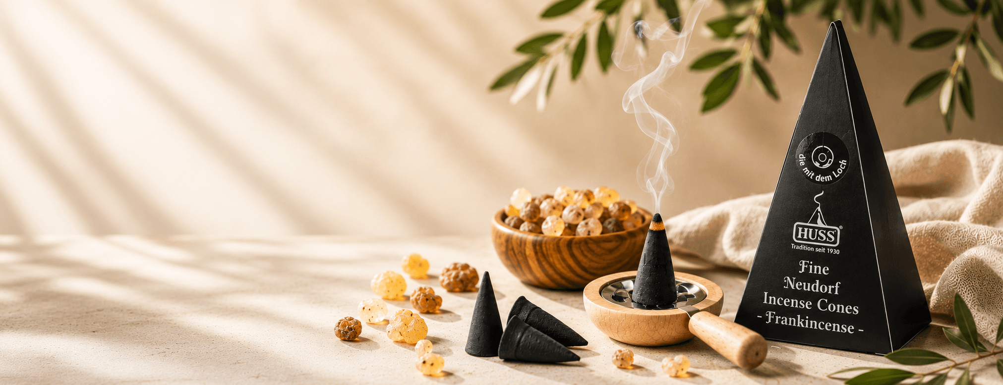 HUSS Incense cone package beside a HUSS Incense smoking pan with a smoking cone, on a draped beige fabric surface and resins in a wooden bowl.