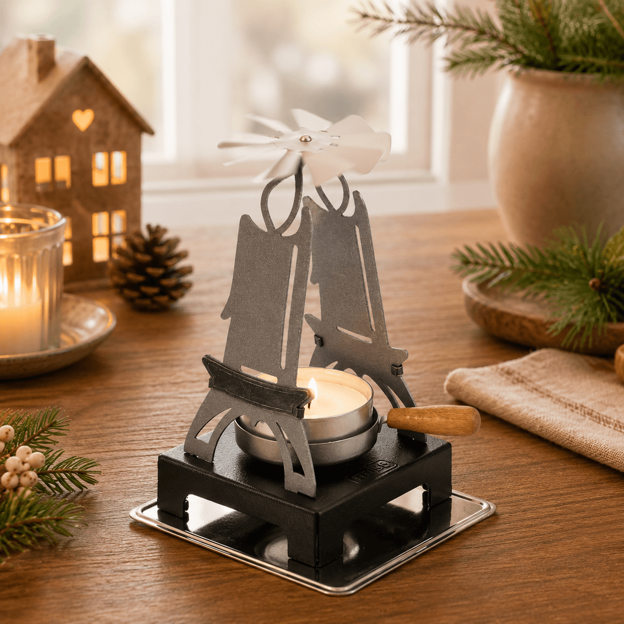 HUSS Incense pyramid candle holder in silver with a lit tealight and spinning white fan displayed on a wooden table with Christmas decor.