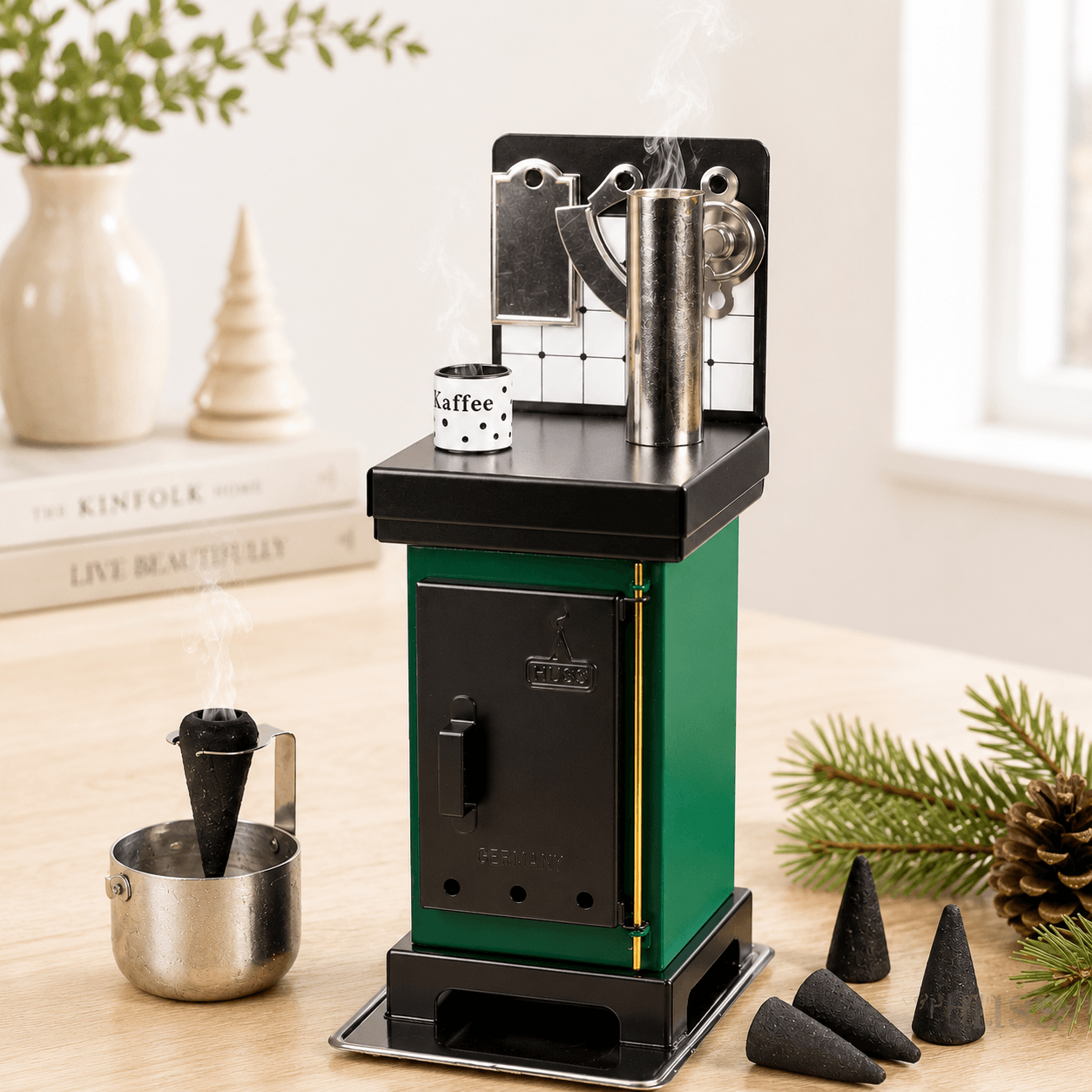 HUSS Incense incense cone oven in green and black with rising steam, displayed on a wooden table in a cozy scene with some Christmas decor.