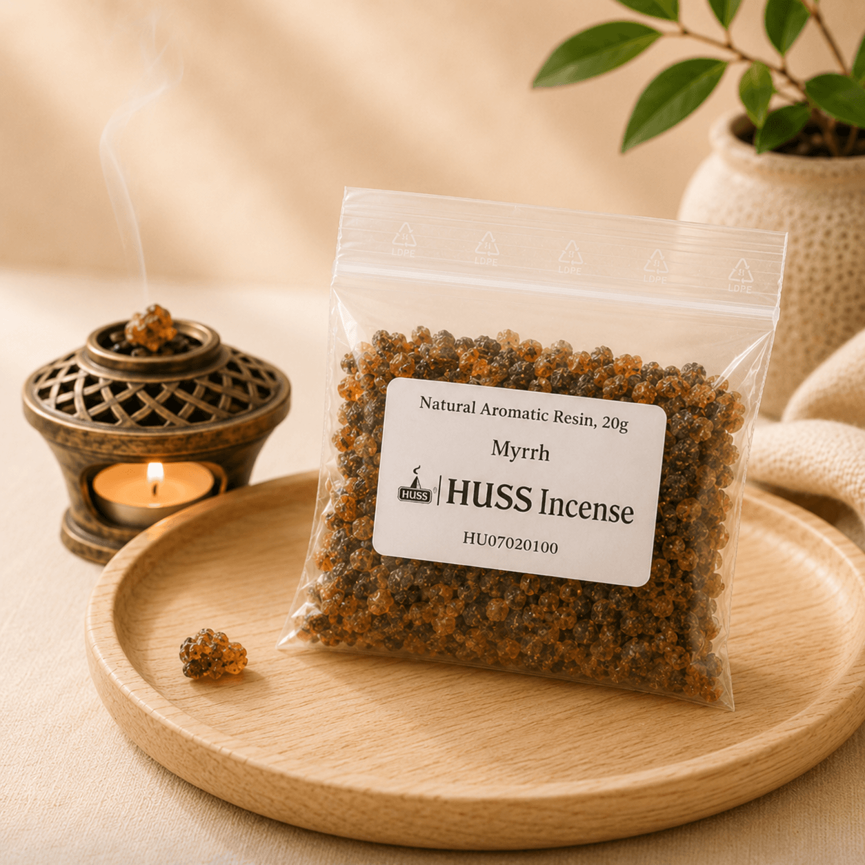 A clear plastic bag of HUSS Incense Myrrh resin sits on a round wooden tray, with a small burning incense burner and a potted plant in the softly lit background.