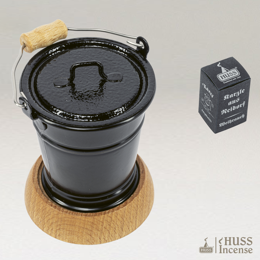 HUSS Incense smoking bucket in black with a lid and a wooden base and Huss Incense packaging on a light gray background.