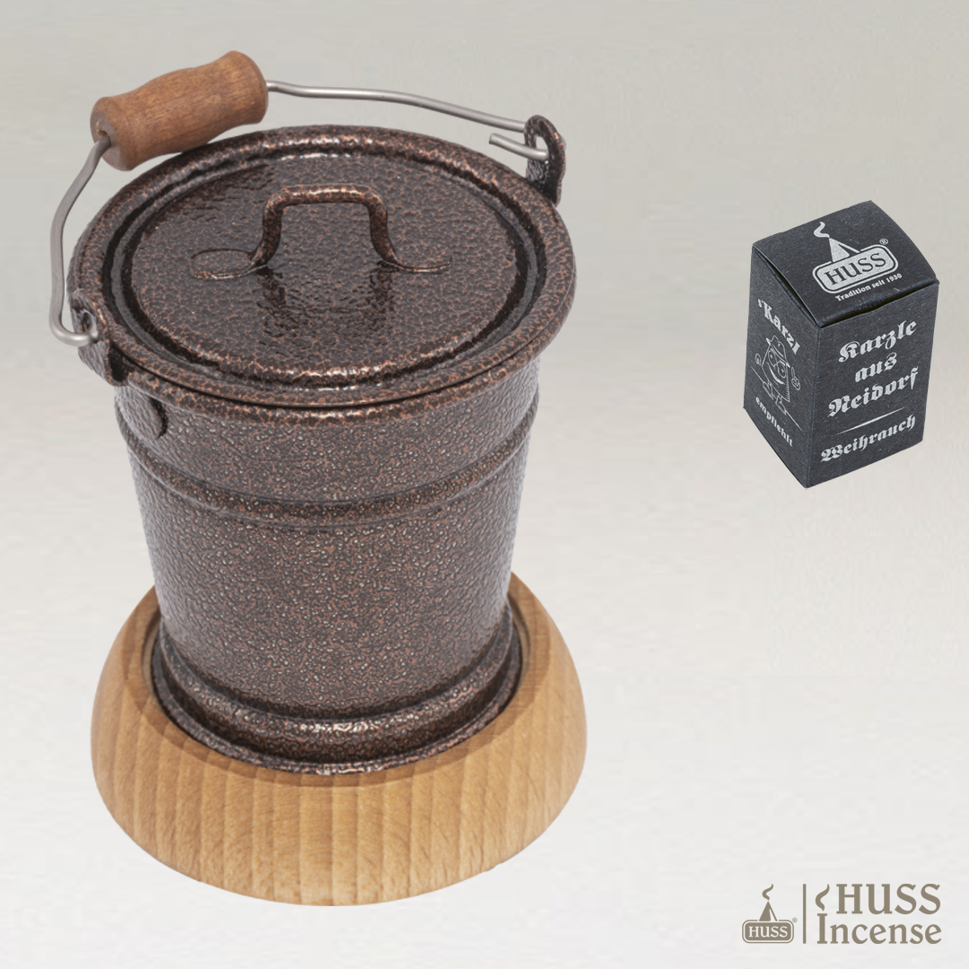 HUSS Incense smoking bucket copper with a wooden base and Huss Incense packaging on a light gray background.