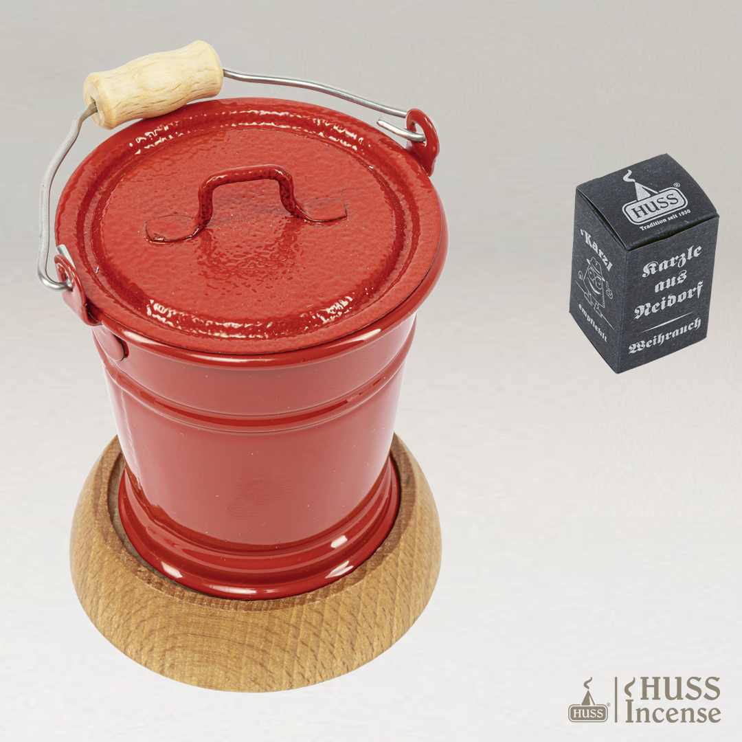 HUSS Incense smoking bucket with closed lid in red on a wooden base and Huss Incense packaging on a light gray background.