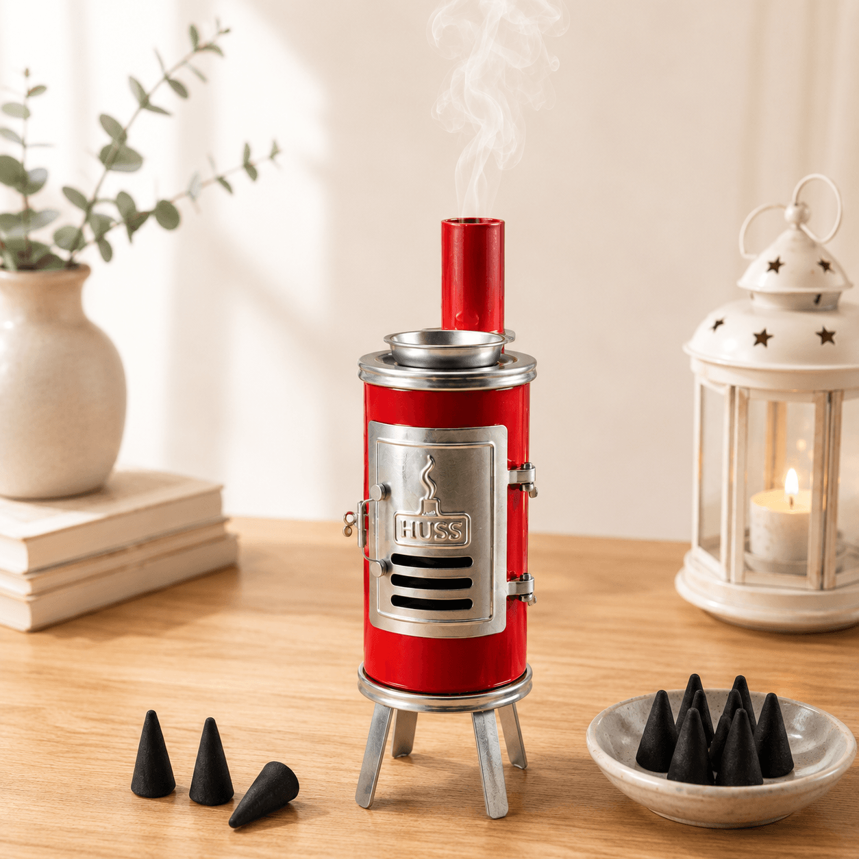 HUSS Incense Glue oven, red with silver accents, smoking chimney, and incense cone holder, displayed on a wooden table with incense cones in a cozy home setting.