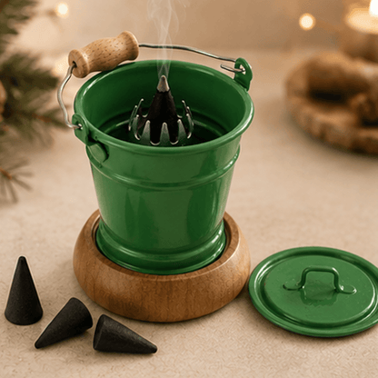 HUSS Incense smoking bucket green with a burning incense cone, removable lid, and loose incense cones displayed in a cozy Christmas scene.