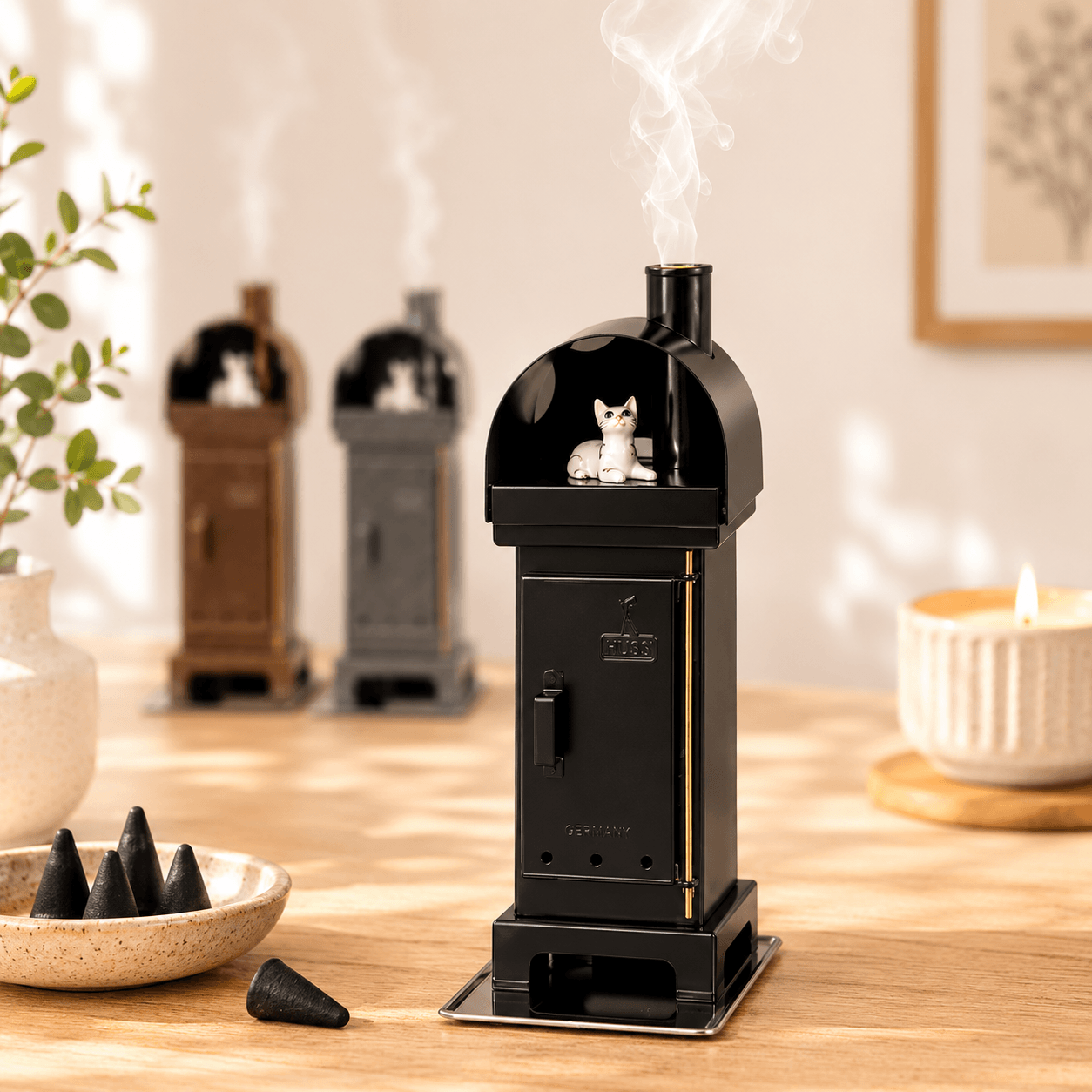Copper HUSS Incense woodburner black with a cat steaming out of the chimney displayed on a wooden table with two more ovens in the back.