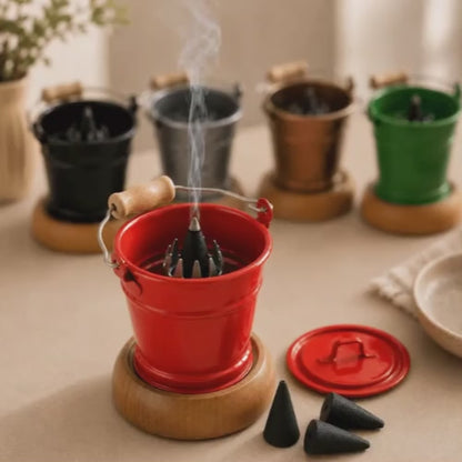Video of a HUSS Incense smoking bucket red with a burning incense cone, removable lid, and loose incense cones displayed on a wooden table with more buckets in the background.