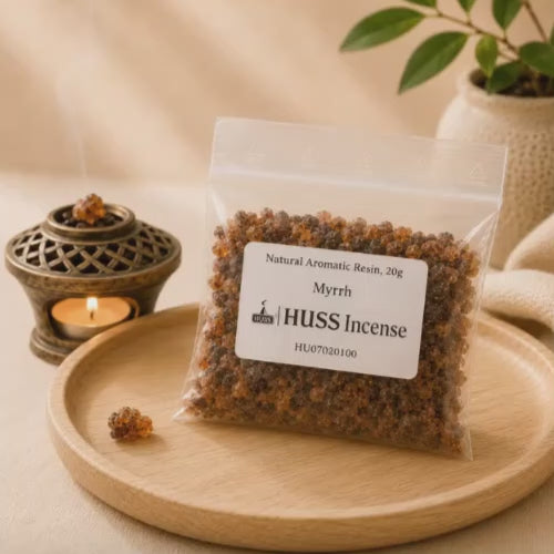 Video of a clear plastic bag of HUSS Incense Myrrh resin sits on a round wooden tray, with a small burning incense burner and a potted plant in the softly lit background.